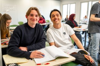 Een docent en een leerling kijken richting de camera