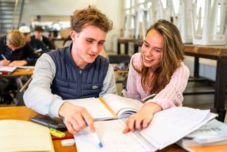 Docent helpt leerling en wijst iets aan in zijn schrift.